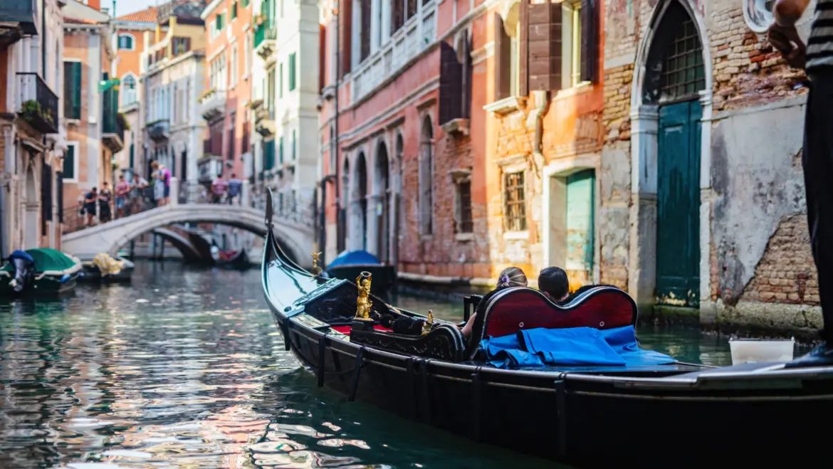 Iconic black gondola drifting across quiet Venetian canal historic buildings Venice Italy