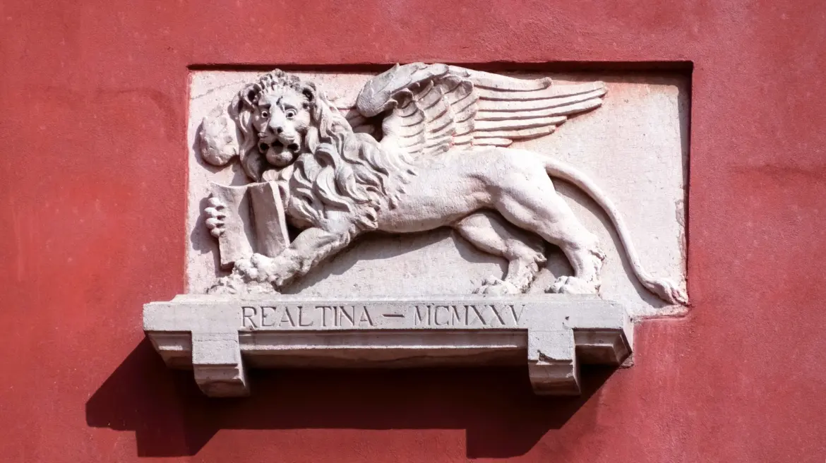 Plaque featuring Winged Lion of Saint Mark mounted red plaster wall above window balcony Venice Italy residential architecture