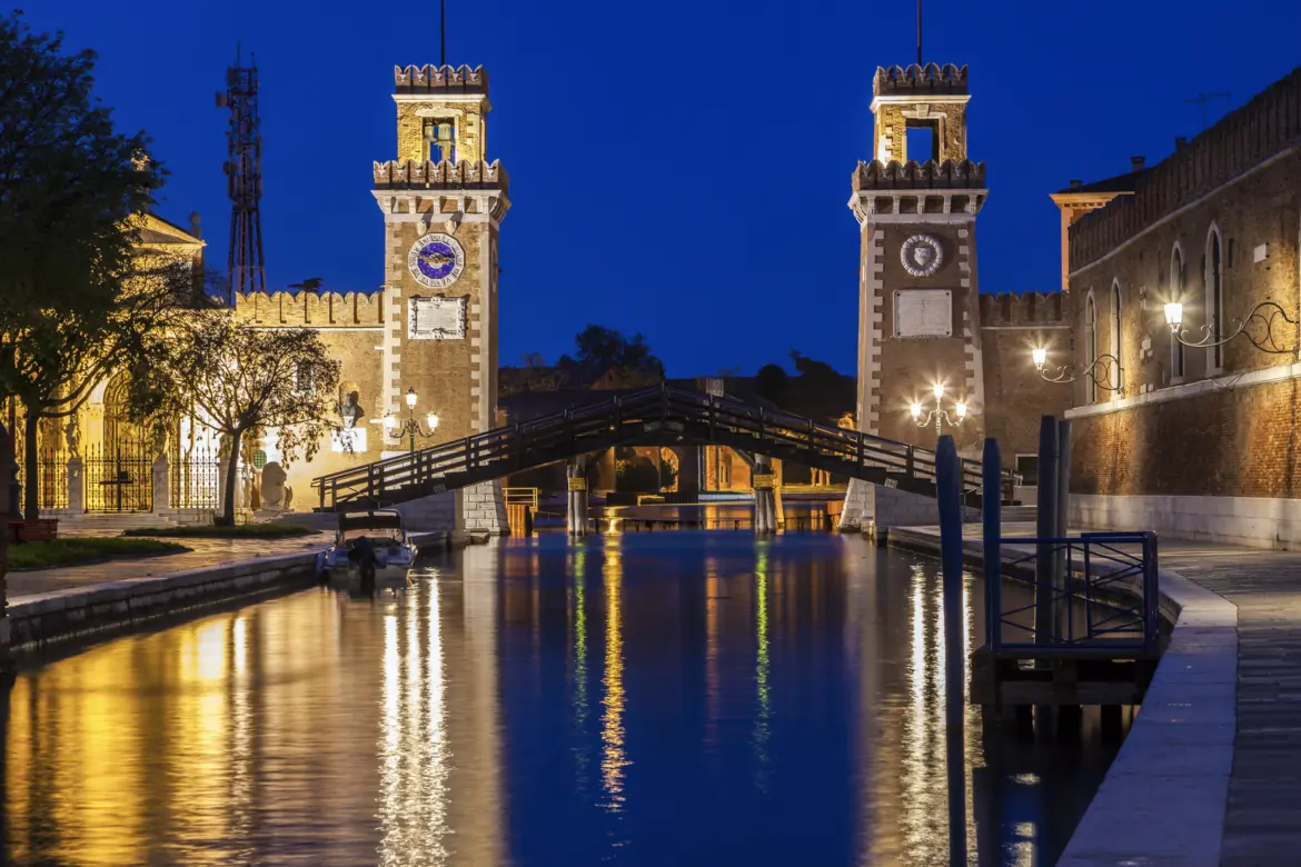Night view historic stone towers Arsenale di Venezia reflected in canal Castello district Venice Italy illuminated after dark former shipyard Venetian Republic