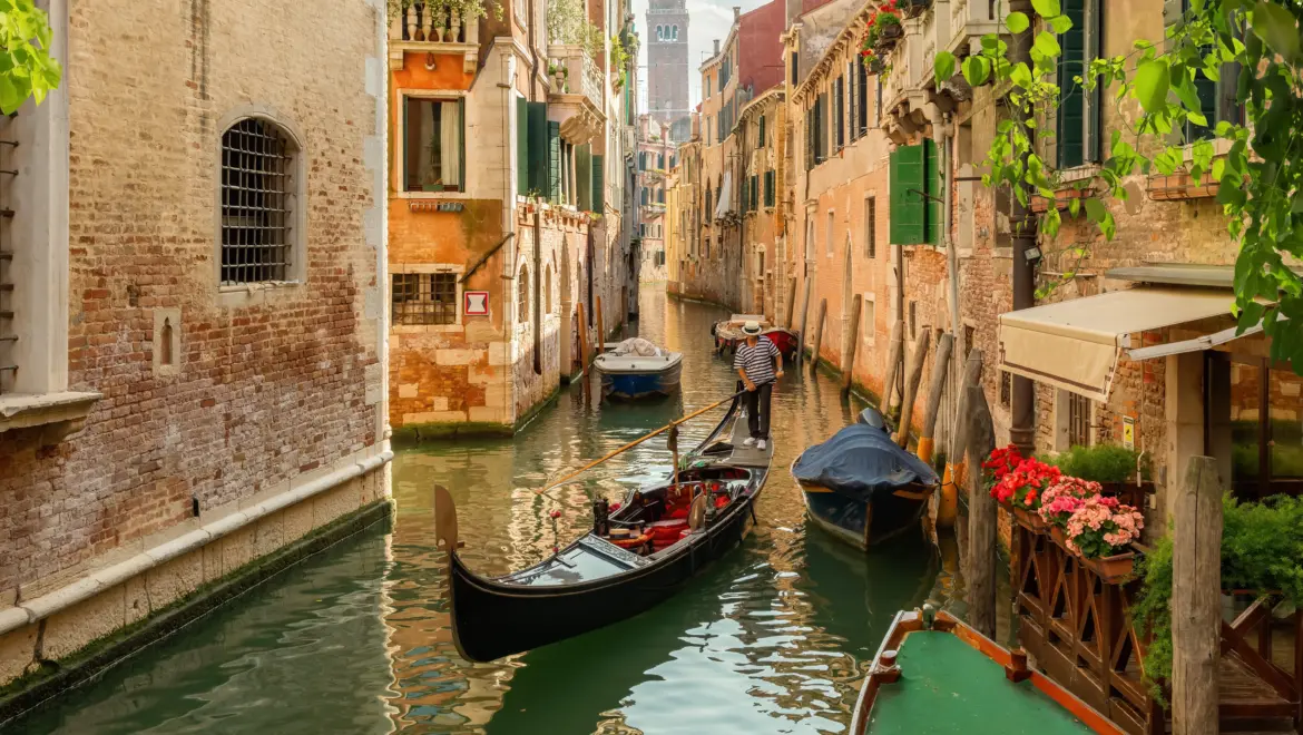 Traditional Venetian gondolier gondolieri navigating gondola through narrow side canal Venice Italy