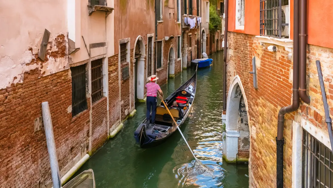 Venetian gondolier gondolieri navigating gondola with tourists along quiet side canal Venice Italy