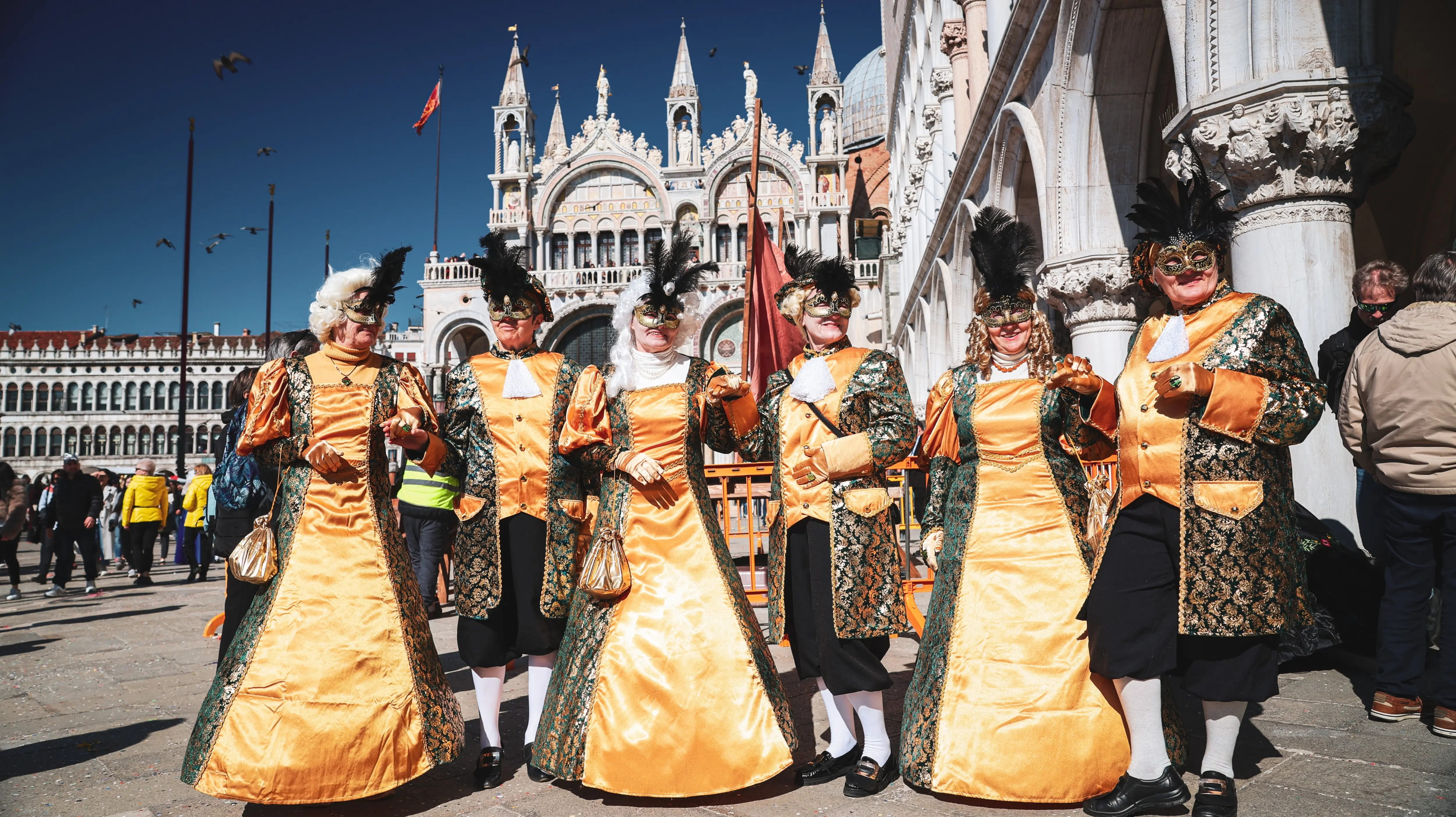 Colorfully dressed participants wearing elegant Venetian Carnival costumes traditional masks gathered Piazzetta San Marco Venice Italy Carnevale di Venezia historic columns ceremonial atmosphere
