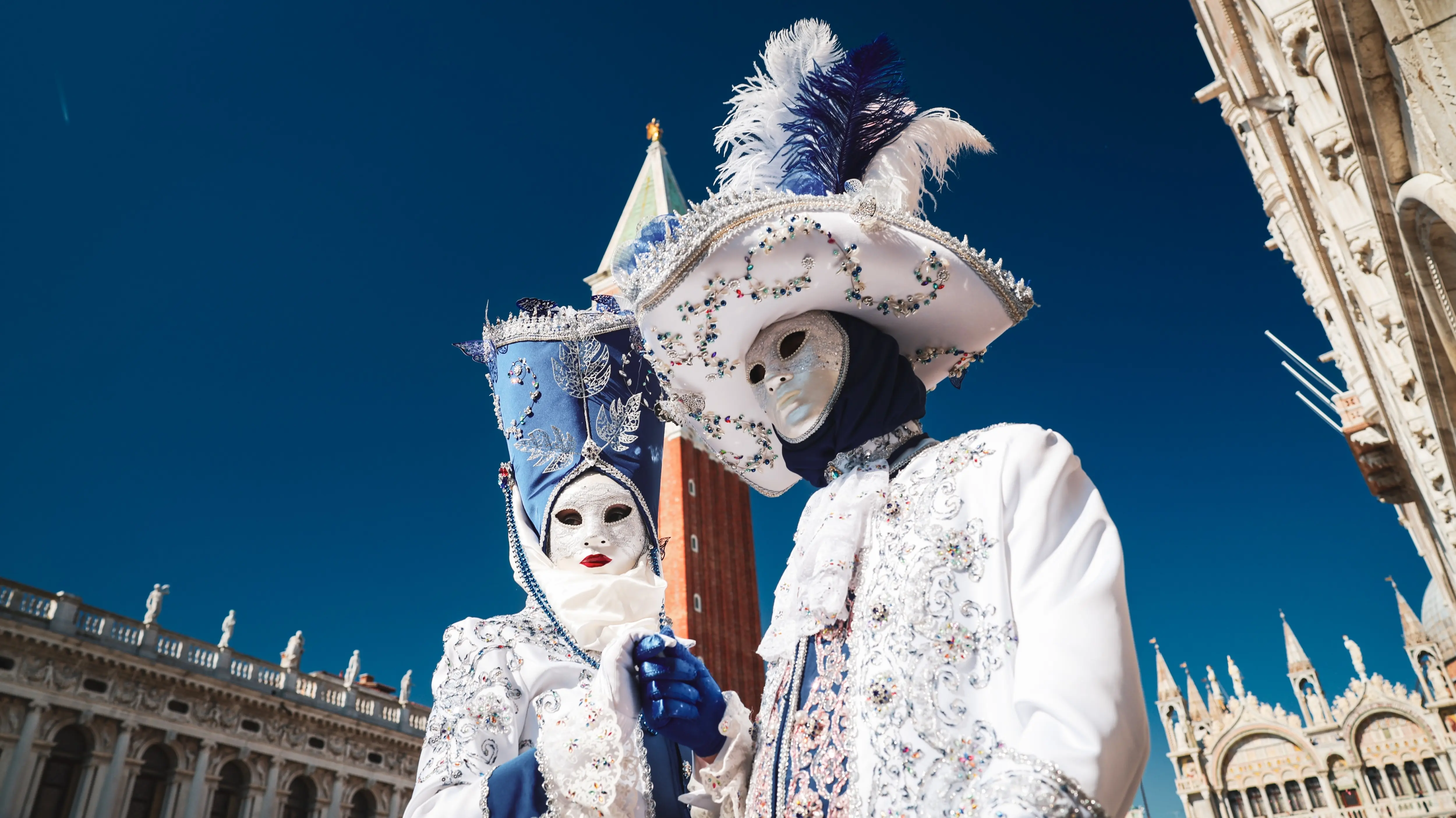 Couple wearing ornate bejeweled Venetian Carnival costumes traditional masks stands Piazzetta San Marco front St Mark's Campanile during Venice Carnival Carnevale di Venezia Venice Italy