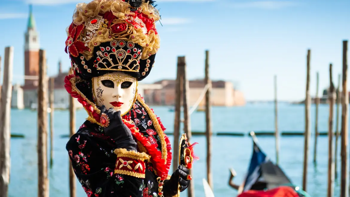 Person dressed traditional Venetian Carnival mask historical attire standing Venetian Lagoon Venice Italy waterfront winter light atmospheric Carnival scene