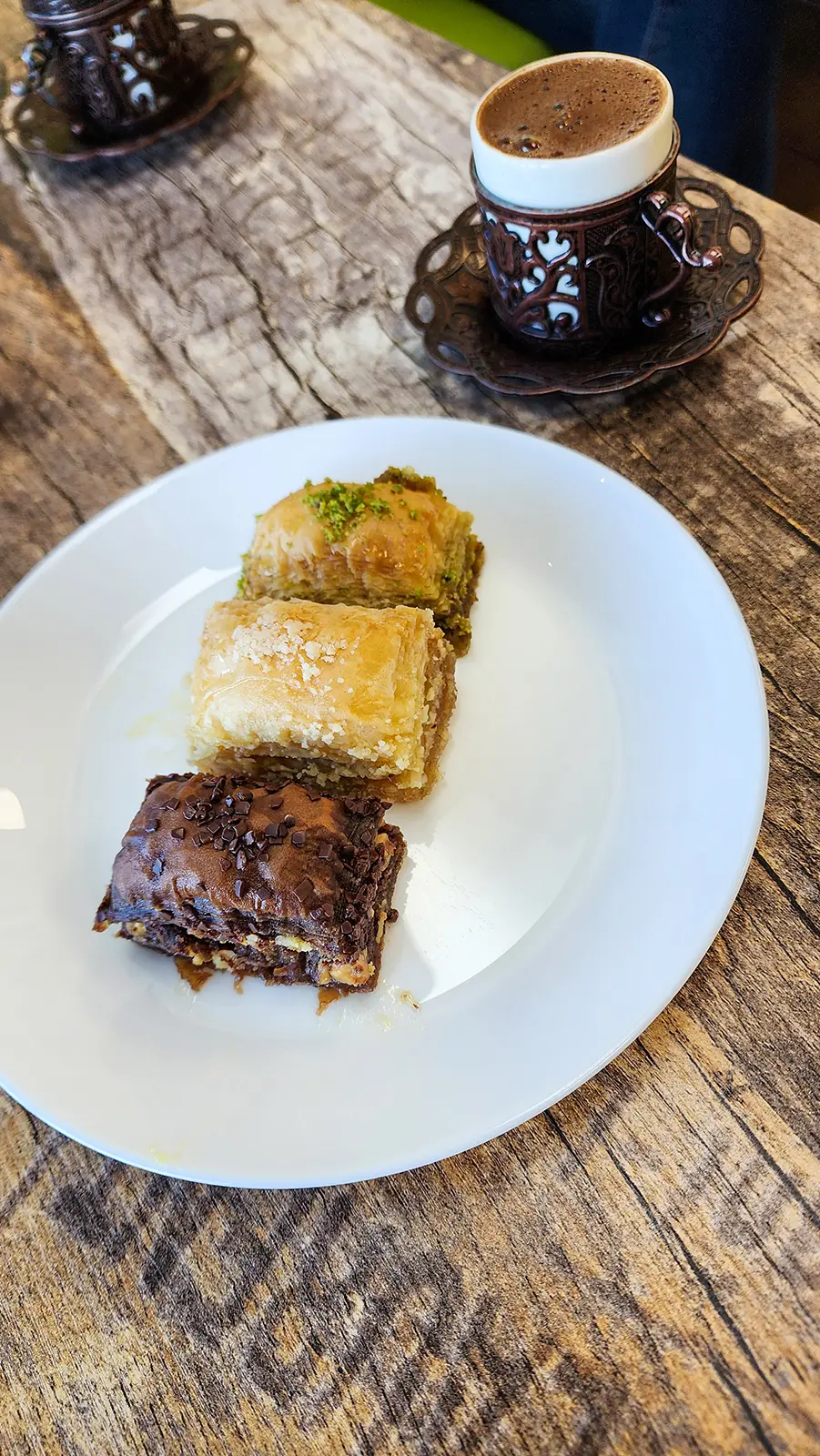 Overhead view of baklava plate with pistachio walnut and chocolate varieties alongside Turkish coffee at The Golden Horn Vancouver