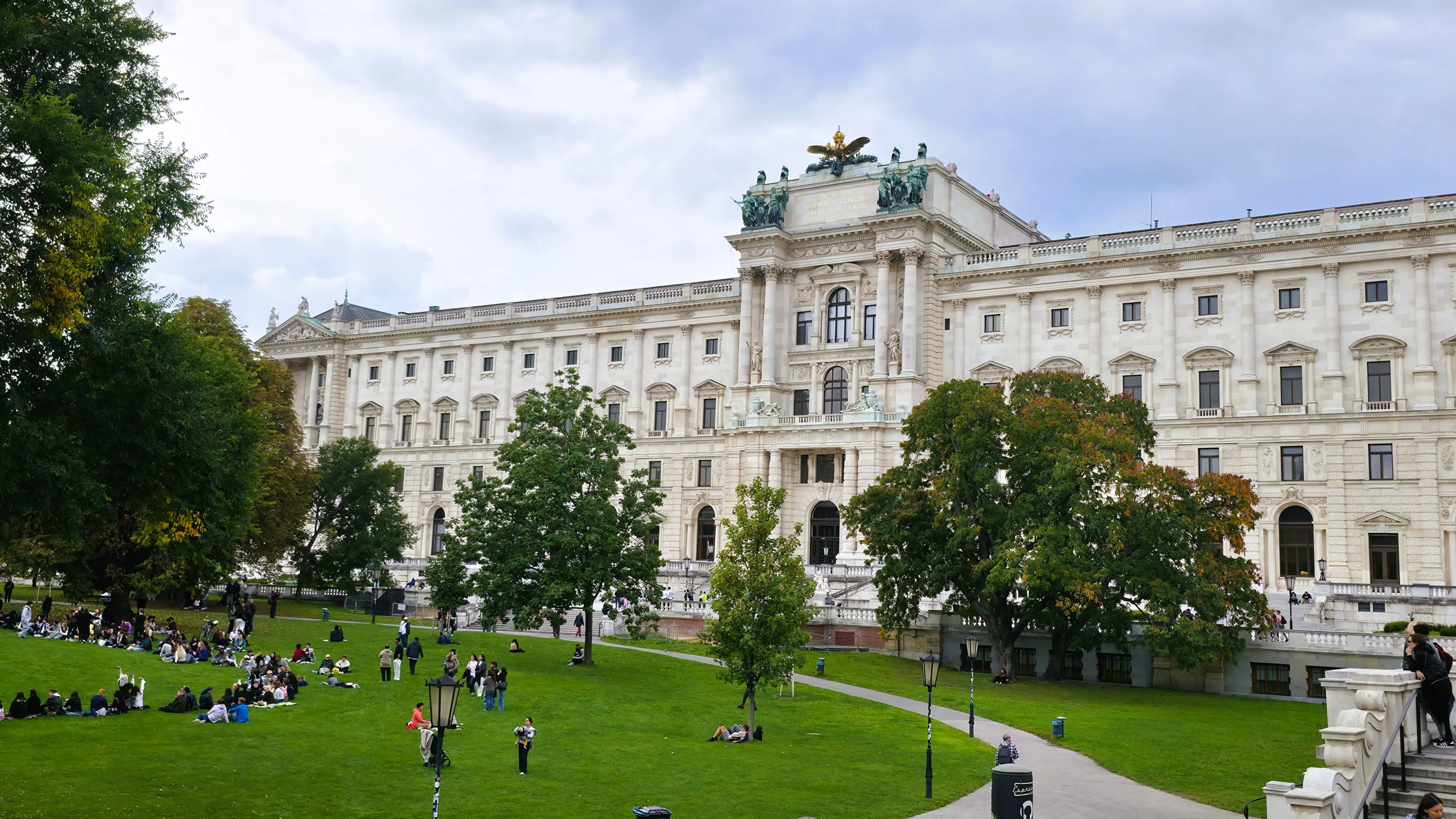 Visitors relaxing on the green lawn of Burggarten in Vienna with the Hofburg Palace in the background