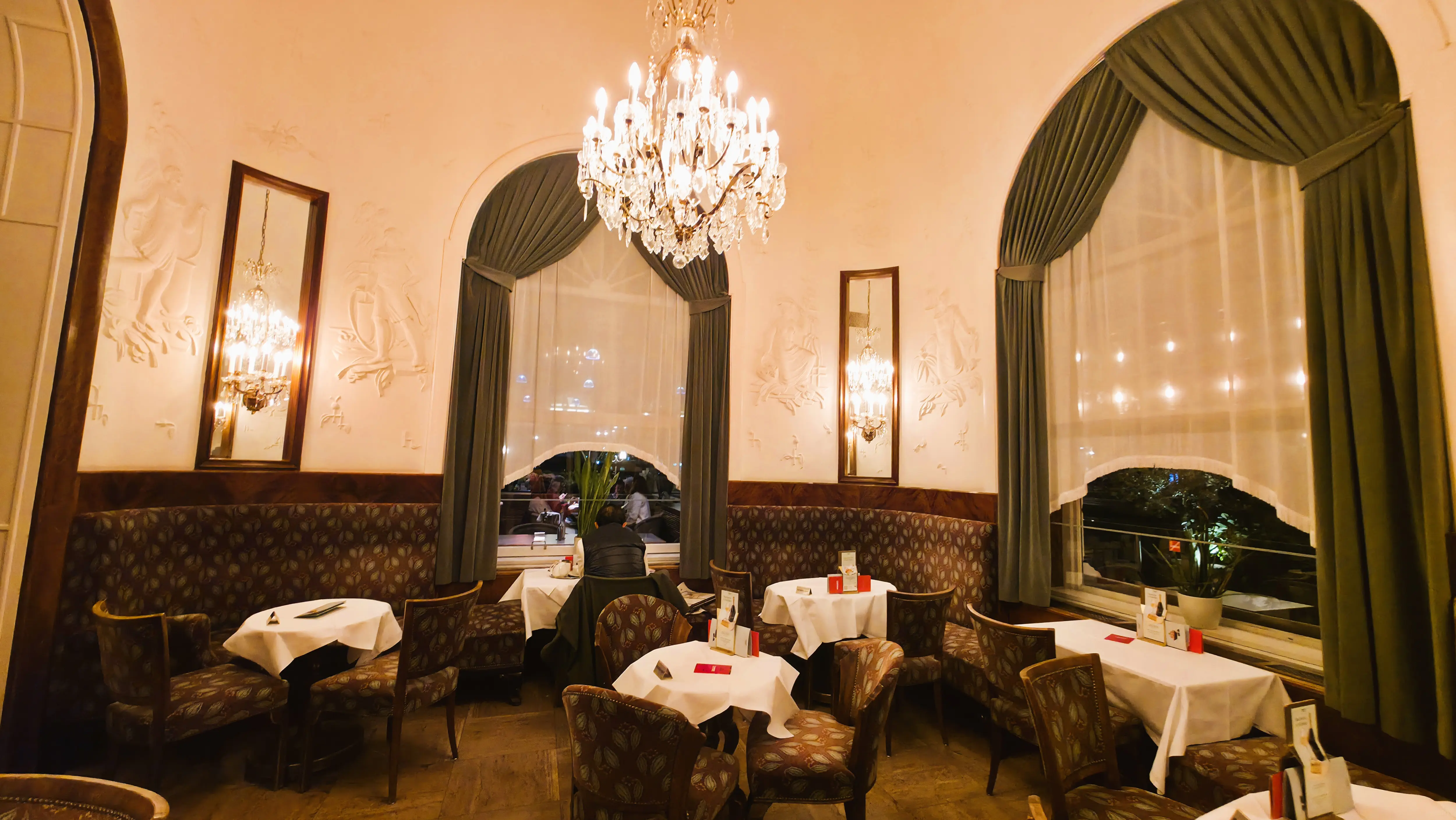 The interior of Café Landtmann in Vienna featuring high ceilings, chandelier, and signature green curtains