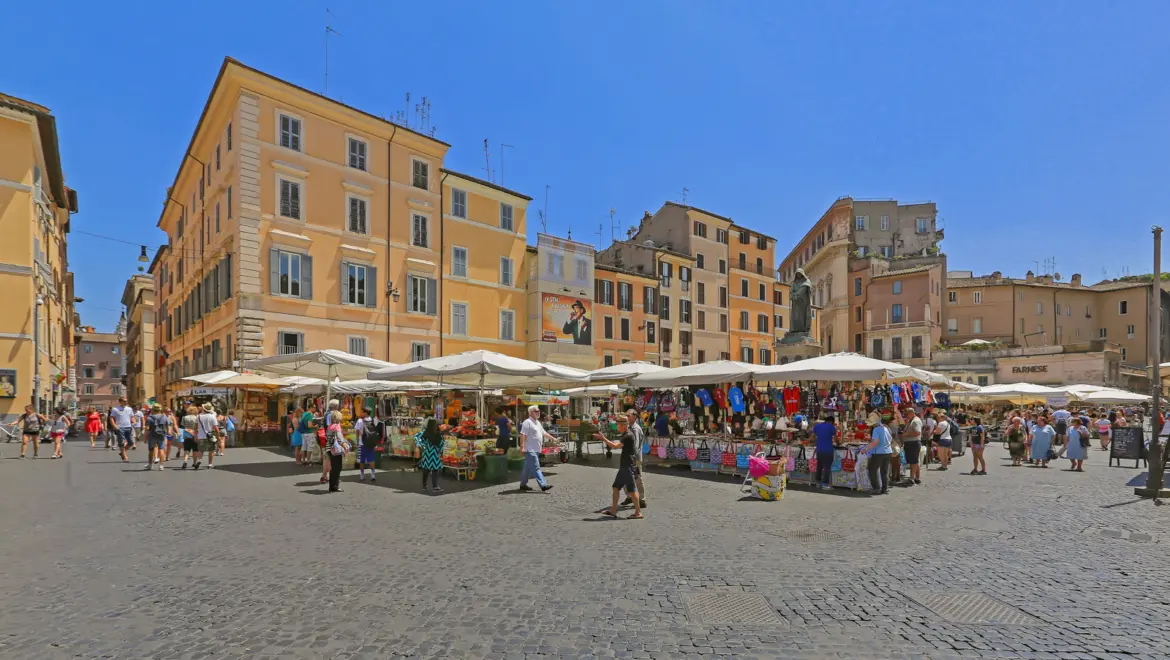 Campo de Fiori market in Rome Italy with colorful vendor stalls surrounded by historic buildings under bright summer sun