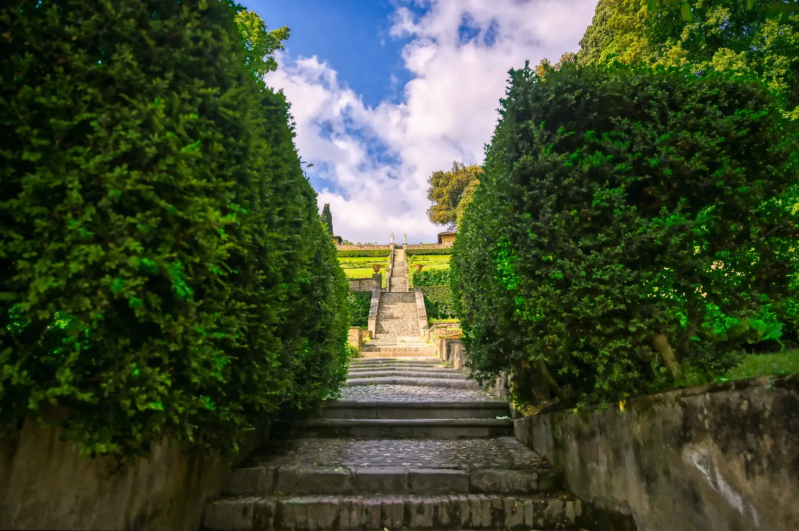 Staircase path through tall cypress trees leading upward through Giardino Bardini in Florence with dramatic sky above