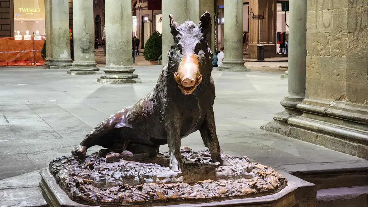 Il Porcellino bronze boar statue at Mercato Nuovo in Florence at night with coins at its base and historic arcade columns