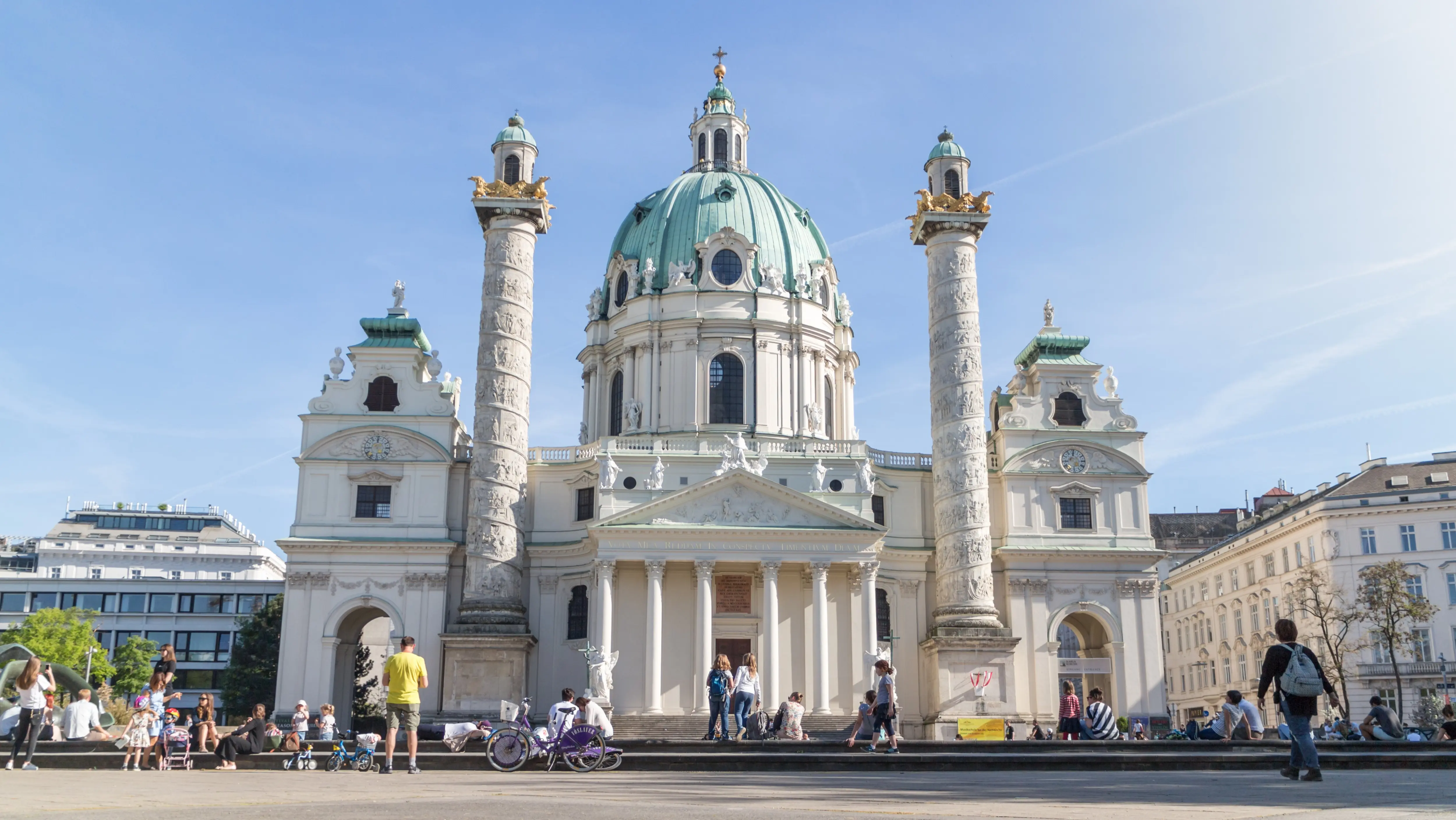 The Karlskirche in Vienna, Austria, with people gathered at Karlsplatz, showing the church as part of everyday city life