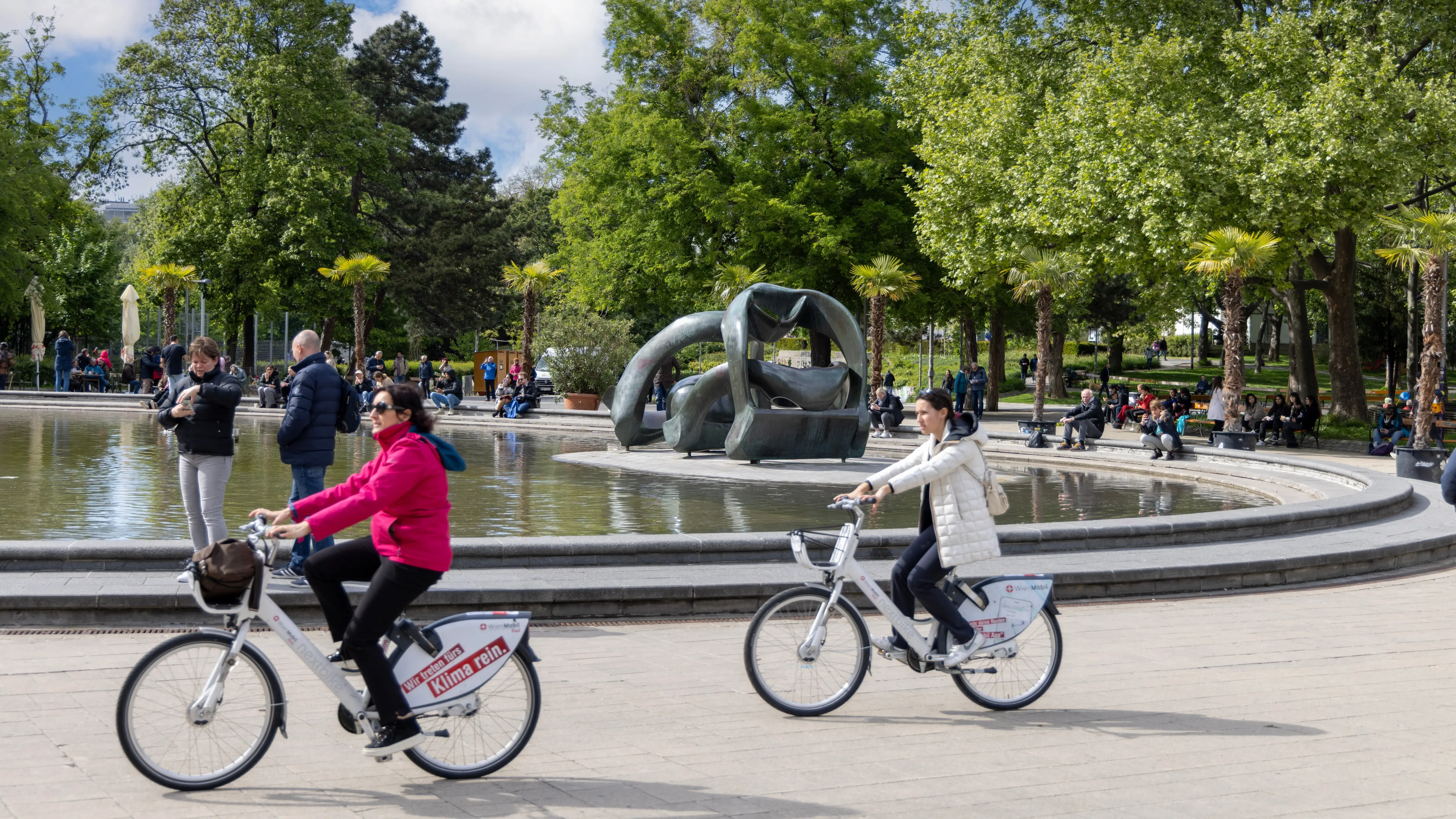 Everyday life at the reflecting pool in Karlsplatz, Vienna, where people pause, cycle, and linger naturally