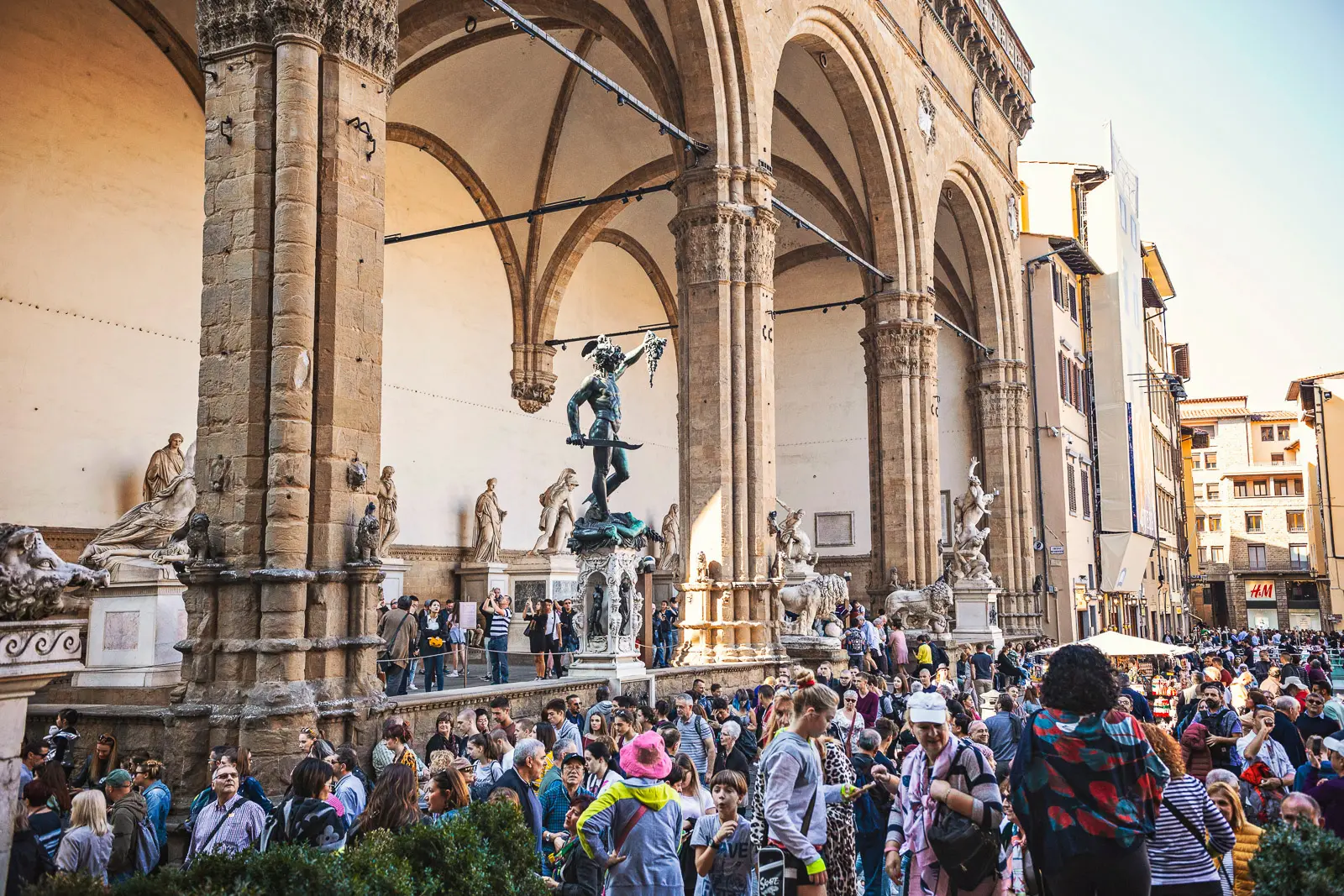 Loggia dei Lanzi in Florence with visitors gathered beneath its Gothic arches viewing the Renaissance sculpture collection in Piazza della Signoria
