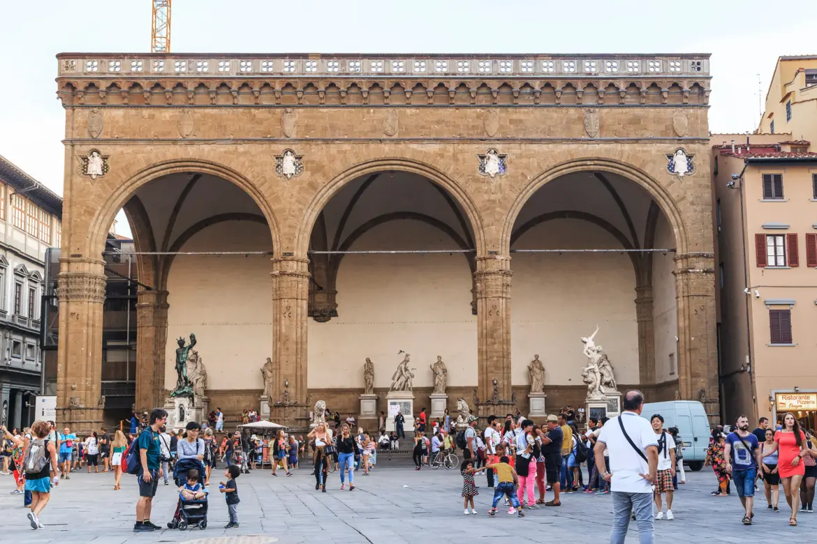 Front view of the Loggia dei Lanzi from Piazza della Signoria in Florence showing the three Gothic arches Renaissance sculptures and visitors in the square