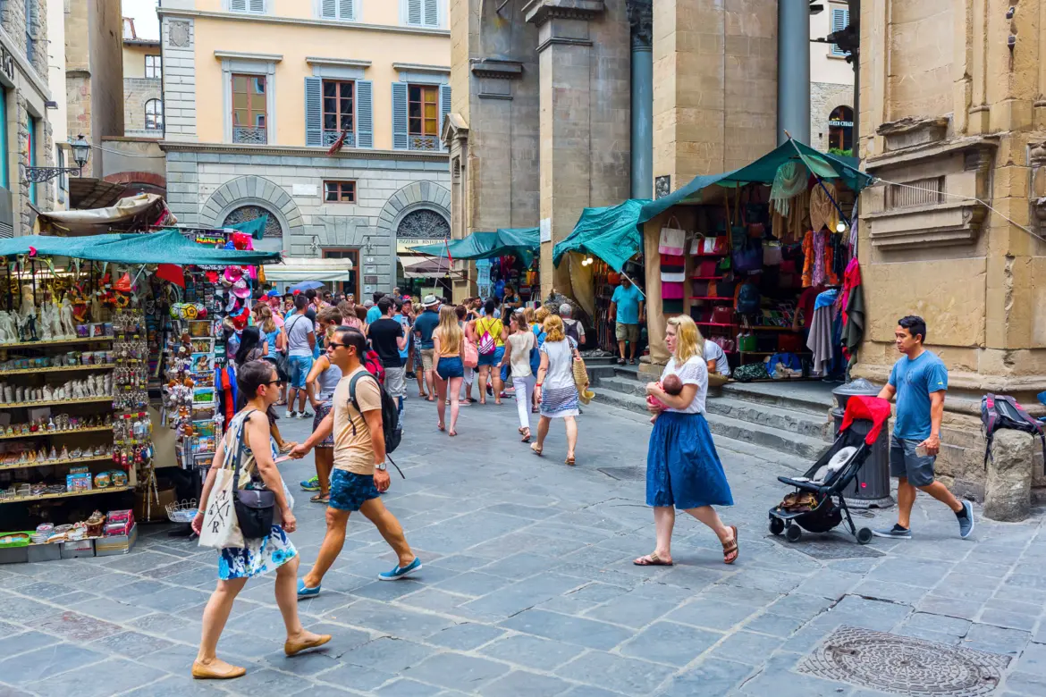 Lively street scene at Mercato Nuovo in Florence with visitors, souvenir stalls, and Renaissance architecture creating the everyday rhythm of the historic center