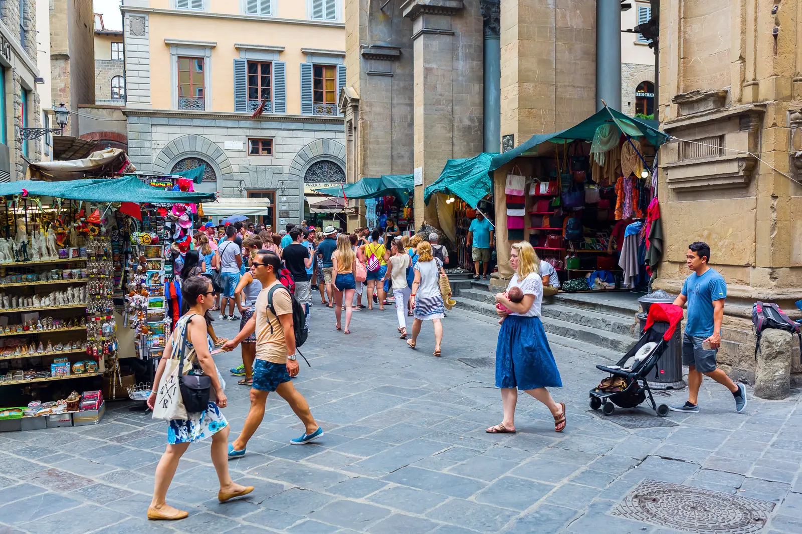 Lively street scene at Mercato Nuovo in Florence with visitors, souvenir stalls, and Renaissance architecture creating the everyday rhythm of the historic center