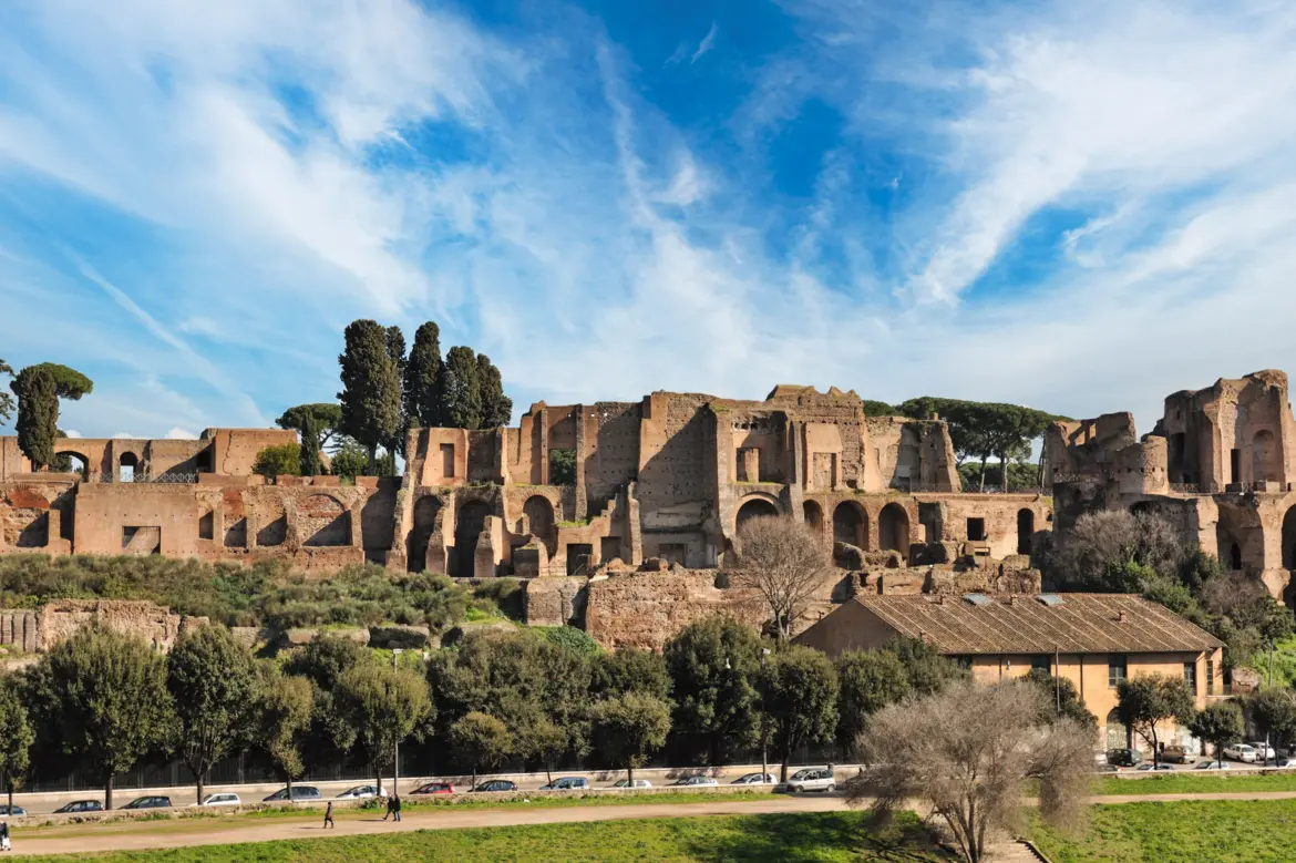 Palatine Hill in Rome Italy showing imperial palace ruins amid gardens and cypress trees with panoramic views under a blue sky with wispy clouds