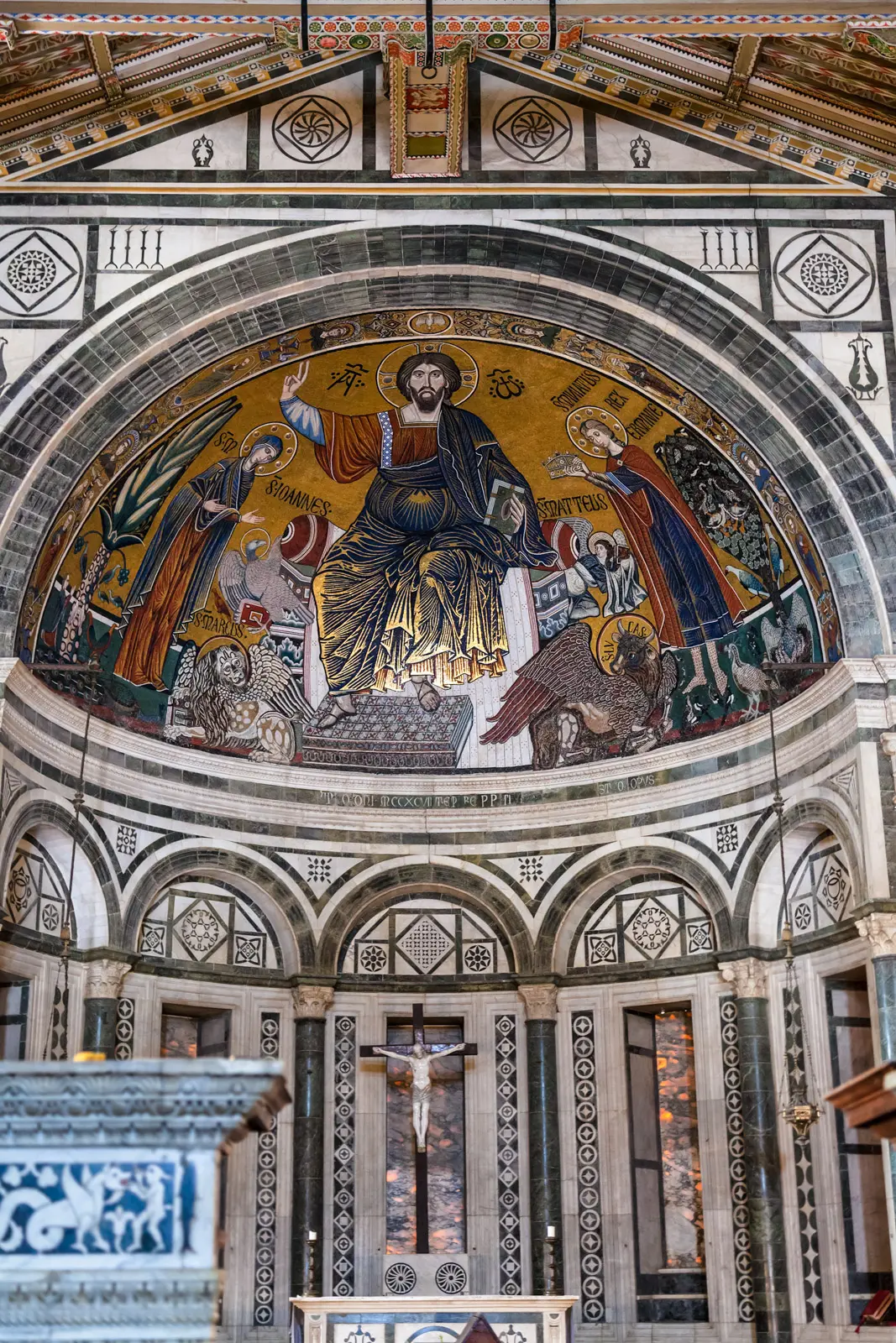 The 13th-century apse mosaic of San Miniato al Monte in Florence depicting Christ enthroned with the Virgin Mary and Saint Miniato, set against a luminous golden background with Byzantine-influenced artistry