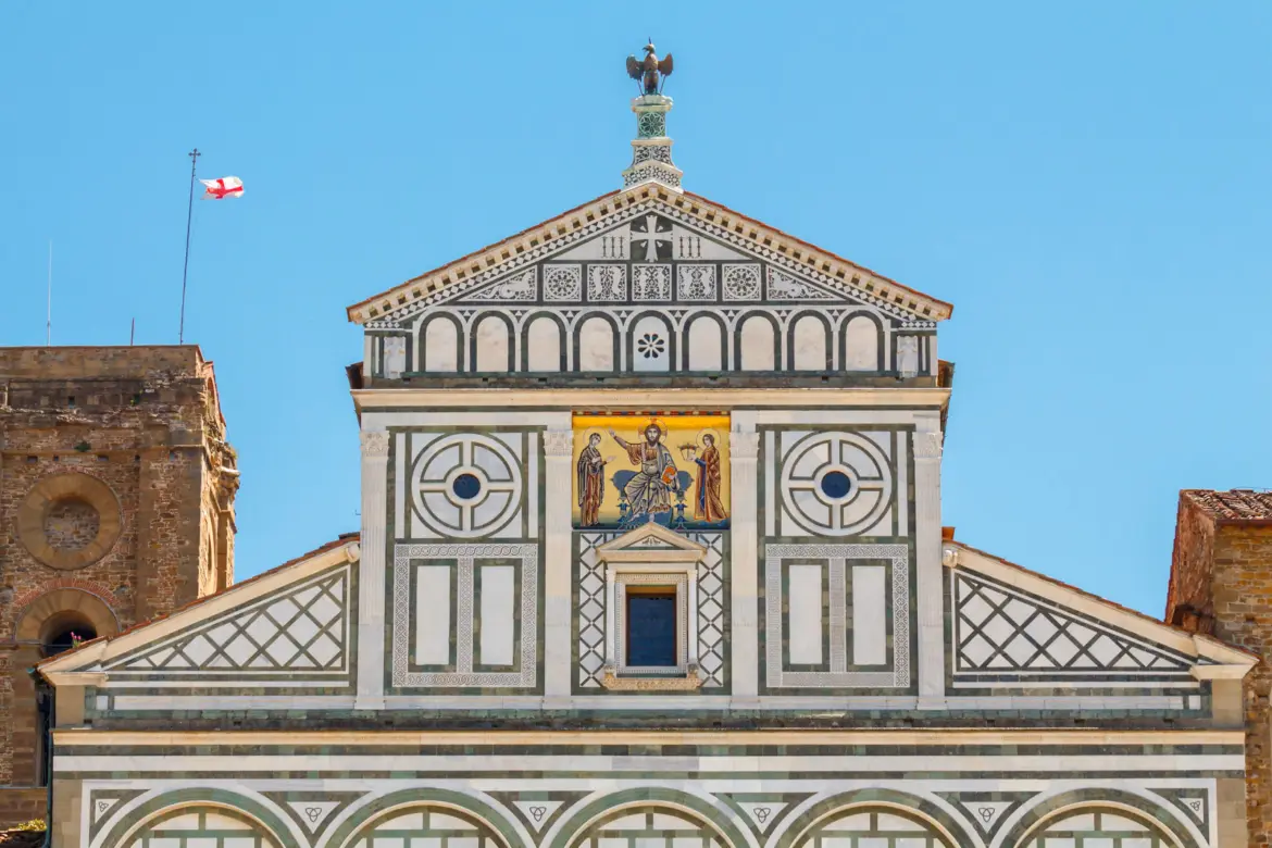 Close-up of the 13th-century golden mosaic on the upper façade of San Miniato al Monte in Florence, depicting Christ enthroned between the Virgin Mary and Saint Minias, crowned by the eagle emblem of the Arte di Calimala guild
