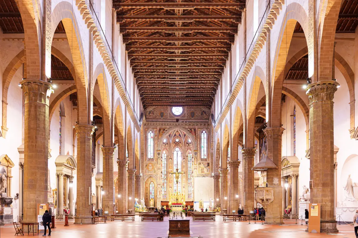 Interior nave of Santa Croce Basilica in Florence with octagonal stone piers timber ceiling and the high altar visible in the distance under warm light