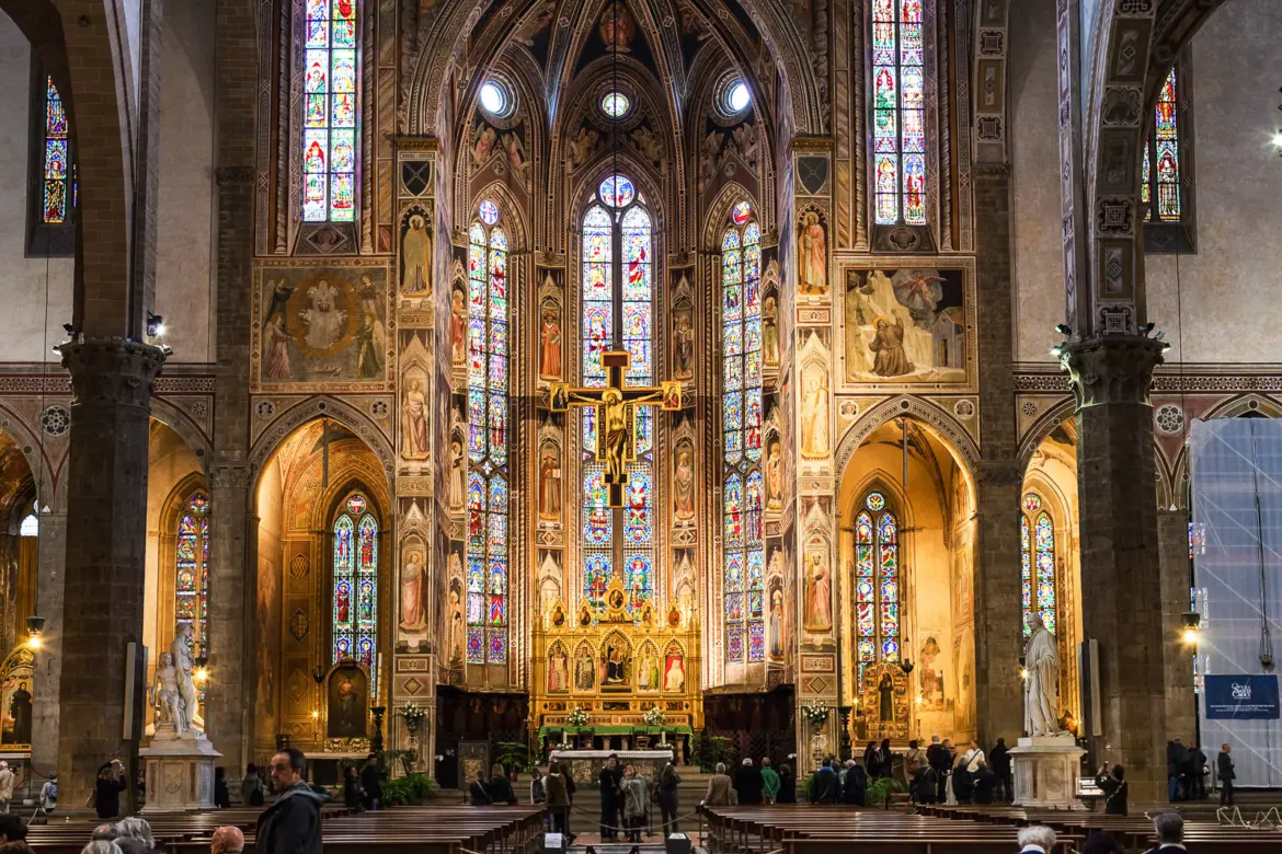 The high altar of Santa Croce Basilica in Florence with glowing stained glass windows frescoes and golden light filling the Gothic apse