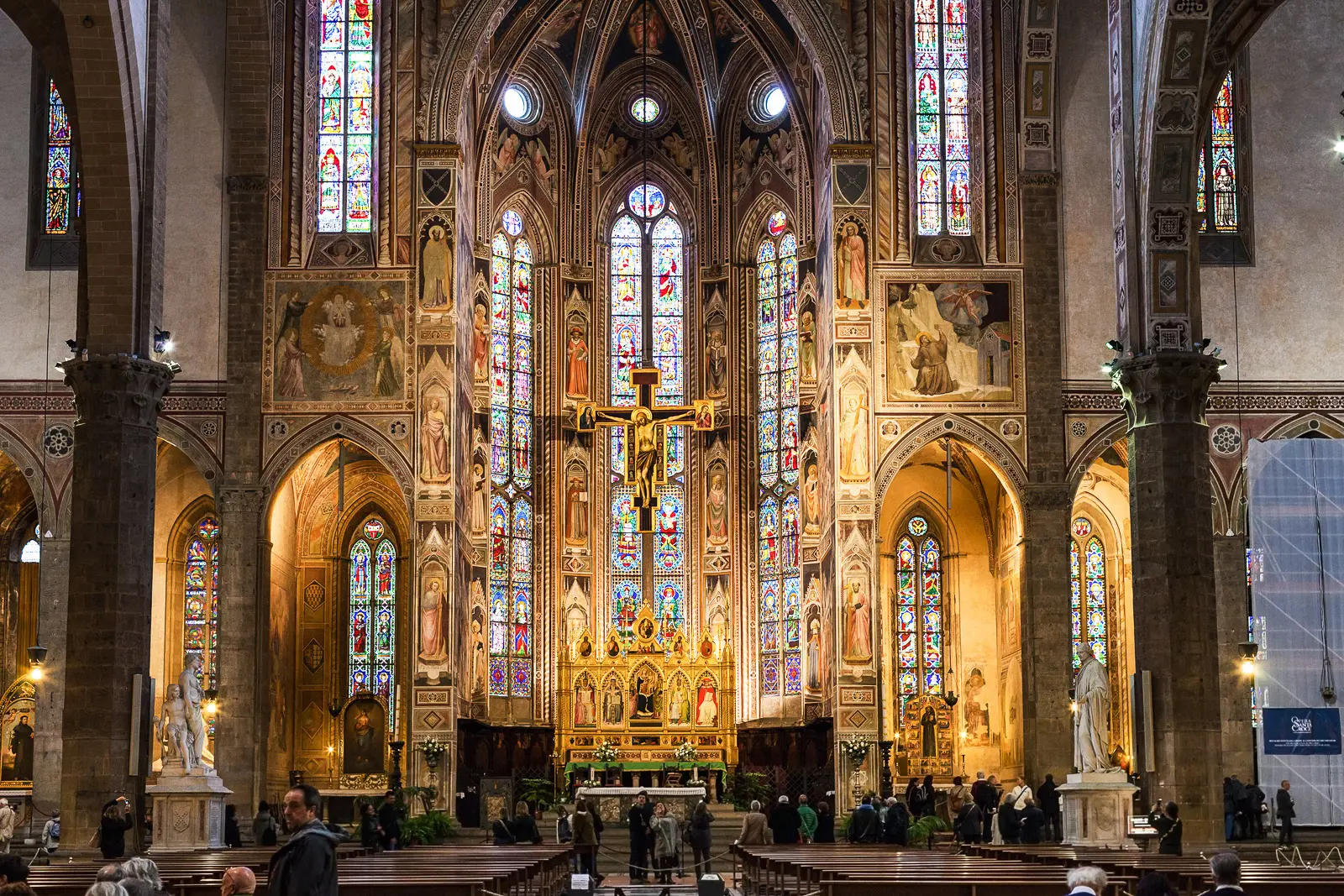 The high altar of Santa Croce Basilica in Florence with glowing stained glass windows frescoes and golden light filling the Gothic apse