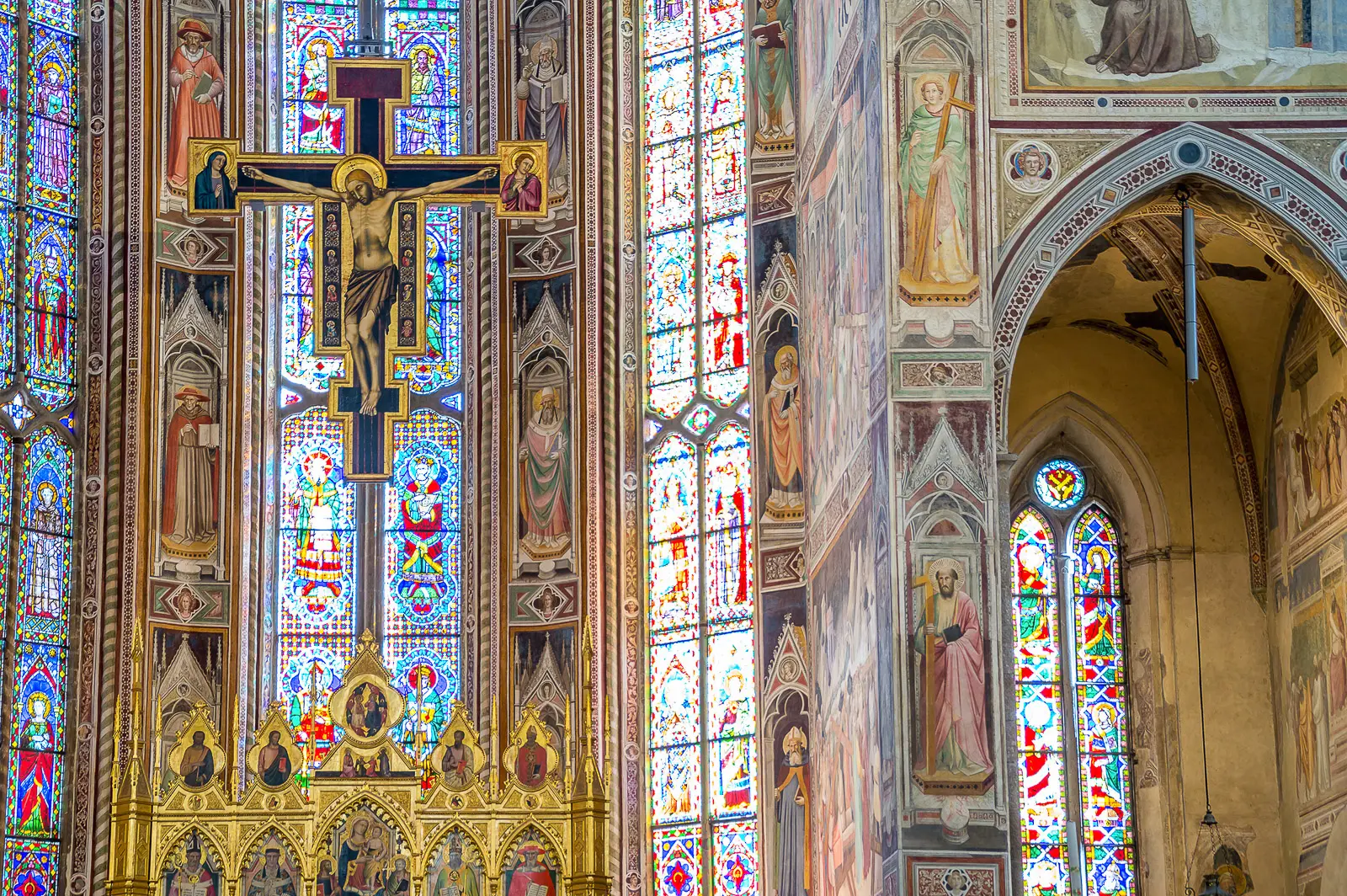 Stained glass windows and crucifix behind the high altar of Santa Croce Basilica in Florence with vivid colors transforming natural light