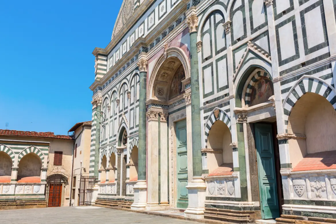 Close-up of Santa Maria Novella’s green and white marble façade in Florence, showing the geometric inlays, classical columns, arched entrance, and heraldic shields designed by Leon Battista Alberti
