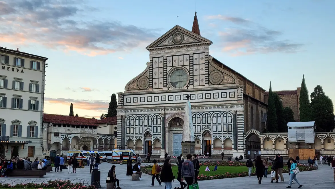 Santa Maria Novella church at sunset seen from Piazza Santa Maria Novella in Florence, with visitors and locals walking through the square in the warm evening light