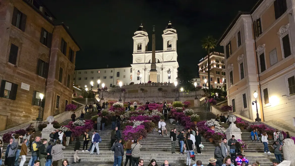 The Spanish Steps in Rome at night with Trinita dei Monti church illuminated at the top and azalea flowers in bloom