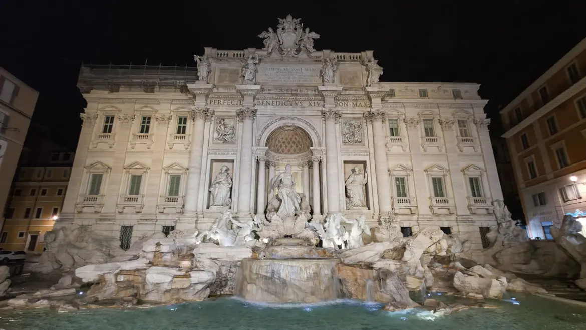 The Trevi Fountain in Rome illuminated at night with golden light on the Baroque marble sculptures and cascading water