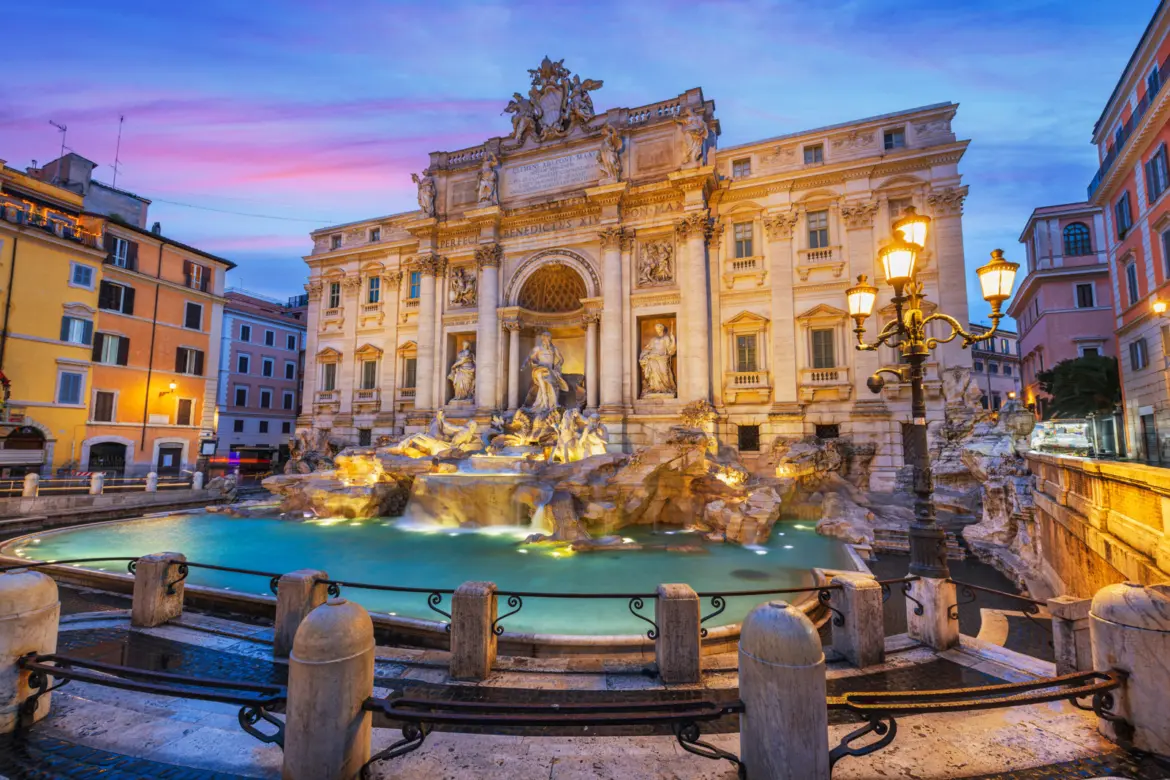 Trevi Fountain in Rome Italy illuminated at twilight with dramatic Baroque sculptures and cascading water against a pink and blue sky