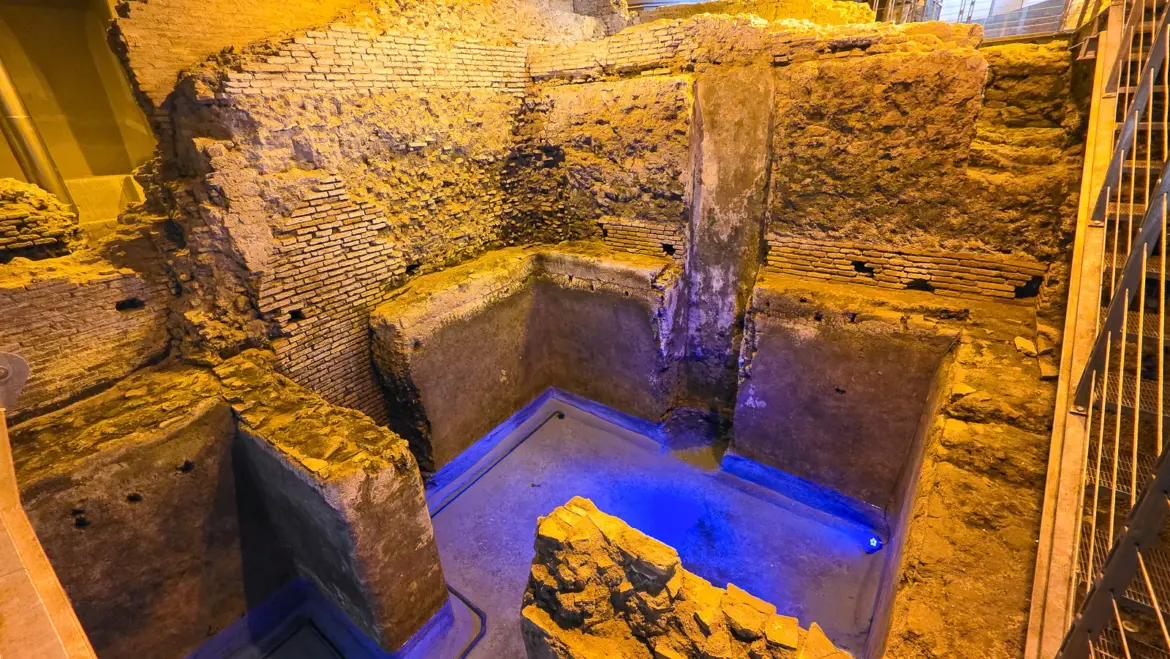 Ancient Roman ruins and water channels inside Vicus Caprarius underground archaeological site beneath the Trevi Fountain in Rome with blue illuminated pool