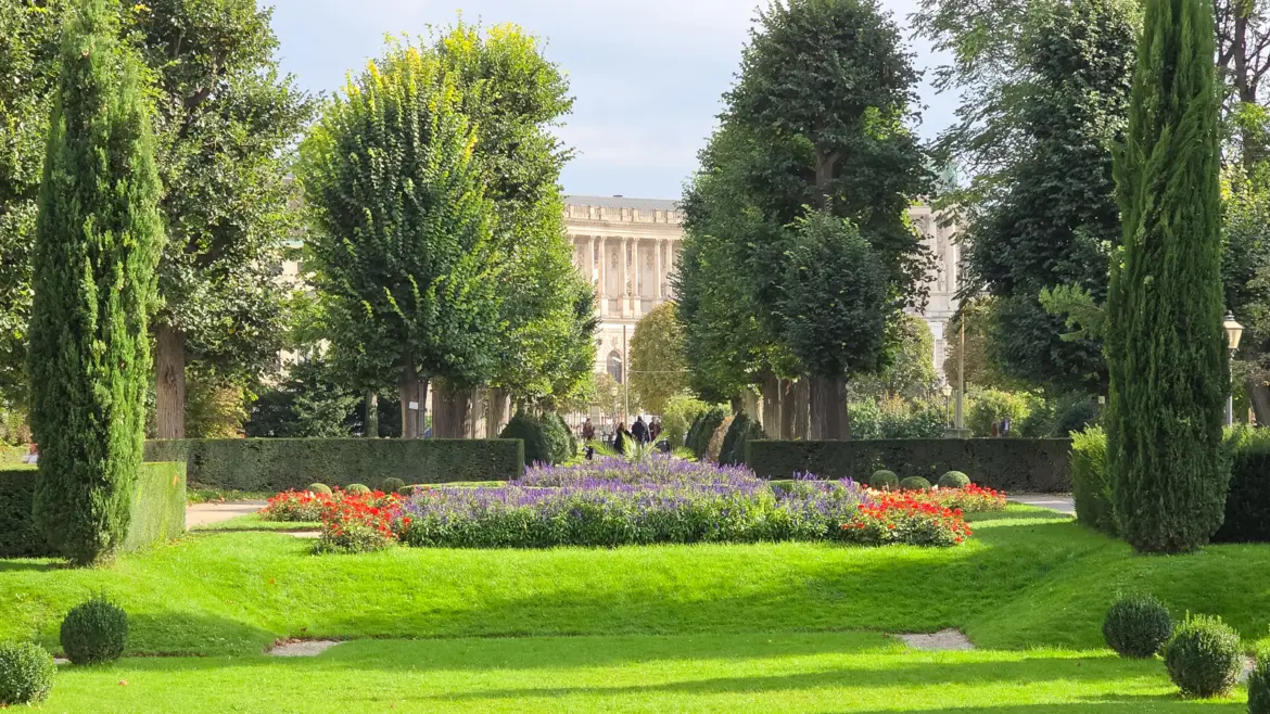 Autumn view Volksgarten Vienna Austria vibrant seasonal colors Hofburg bordering garden fresh greenery blooms formal paths imperial architecture natural beauty