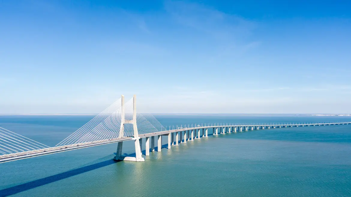 Aerial view of the Vasco da Gama Bridge stretching 17.2 km across the Tagus River in Lisbon with cable-stayed pylons and blue sky