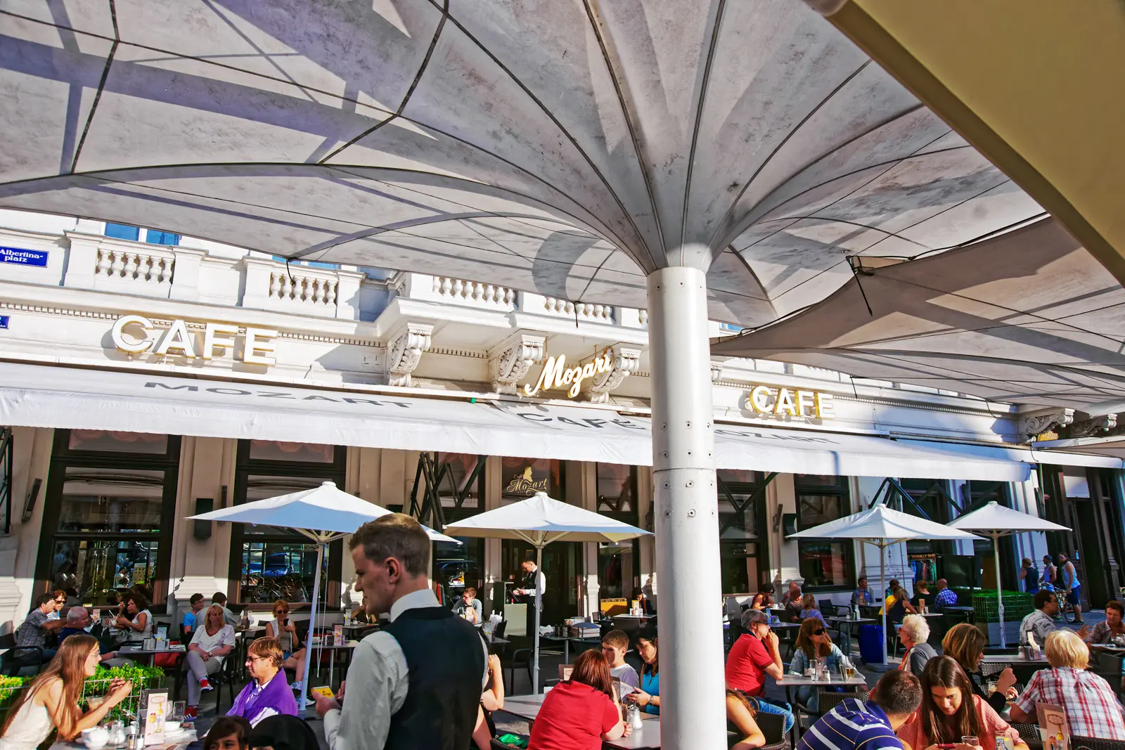 People enjoying outdoor seating at Café Mozart on Albertinaplatz in Vienna, a historic café named after the composer