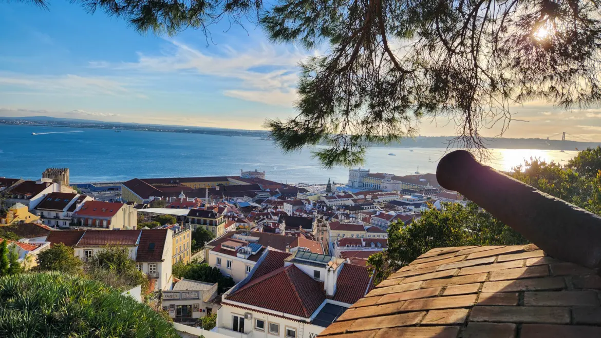 Panoramic view of Lisbon and the Tagus River from Castelo de São Jorge at golden hour with a historic cannon in the foreground