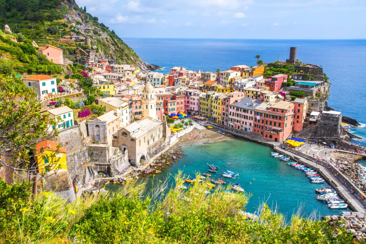 The picturesque coastal village of Vernazza in Cinque Terre with its colorful harbor, dramatic cliffs, and green terraced hillsides overlooking the Ligurian Sea