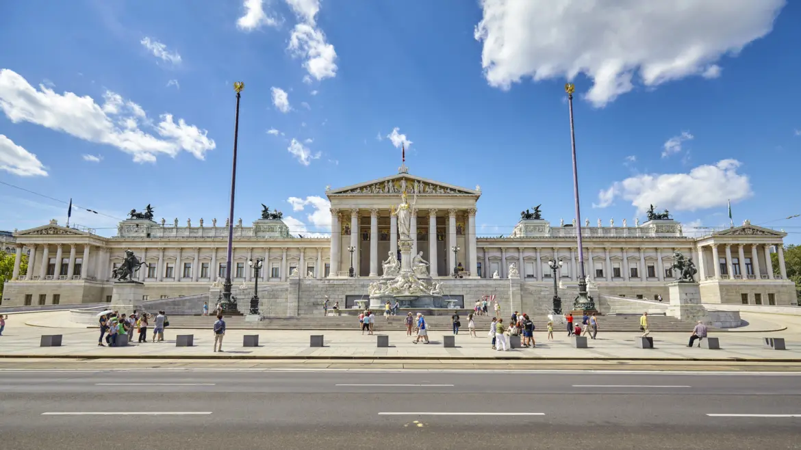 Front façade of the Austrian Parliament Building in Vienna with classical columns and statues along the Ringstrasse