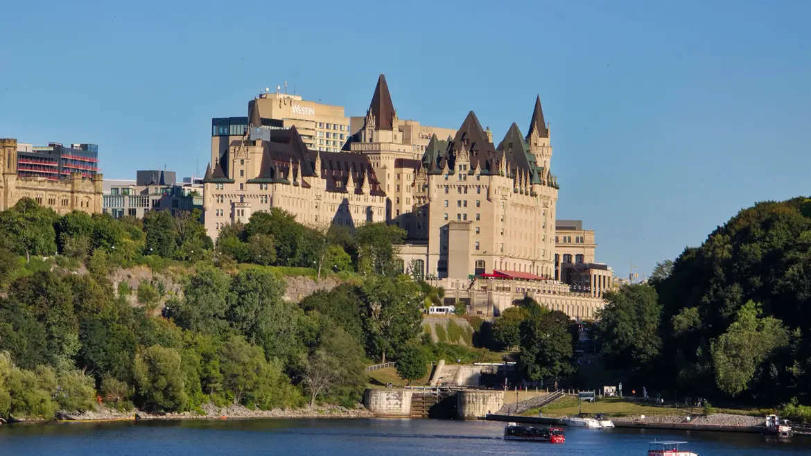 Fairmont Château Laurier rising above the Ottawa River in summer, with its French Gothic limestone turrets and Parliament Hill behind