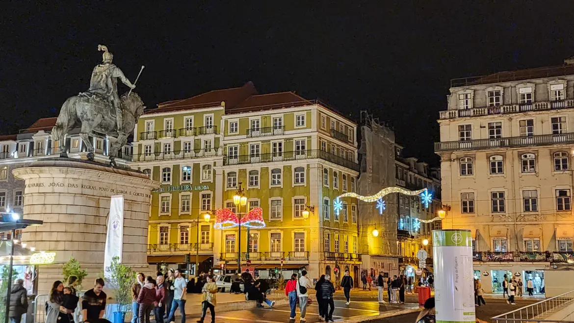 Figueira Christmas Gourmet festival at Praça da Figueira in Lisbon at night with holiday lights, crowds, and the equestrian statue