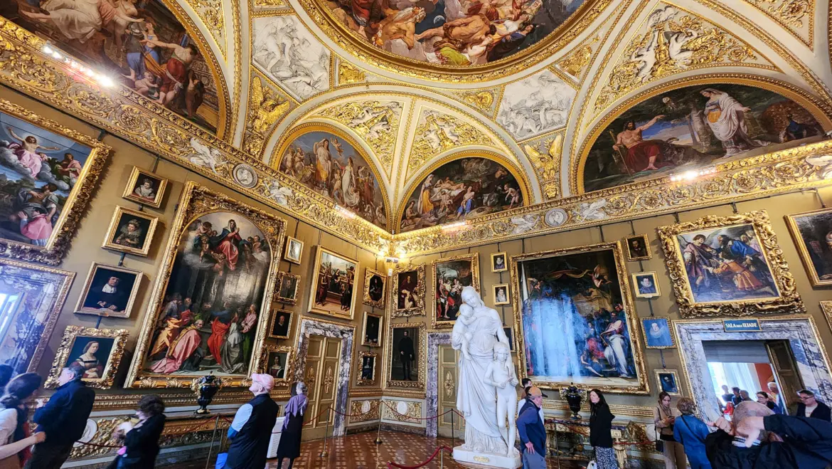 The Palatine Gallery inside Pitti Palace in Florence, with lavishly decorated rooms filled with Renaissance paintings, gilded frames, and ceiling frescoes