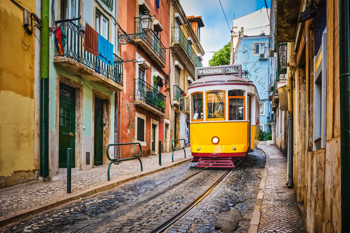 Yellow Tram 28 squeezing through a colorful narrow street with pastel houses and cobblestones in Lisbon