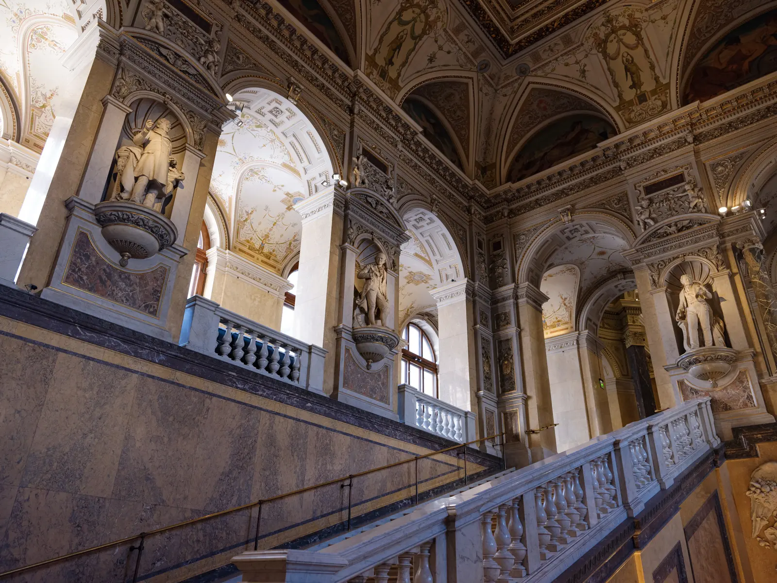 The ornate interior of the Naturhistorisches Museum Wien showcasing the grand staircase, classical sculptures, and architectural grandeur