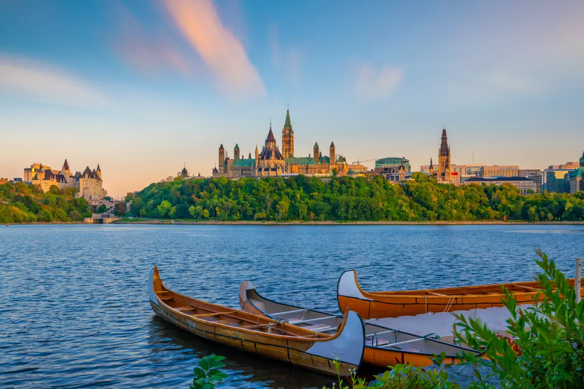 Parliament Hill in Ottawa viewed from across the Ottawa River at golden hour with traditional canoes in the foreground
