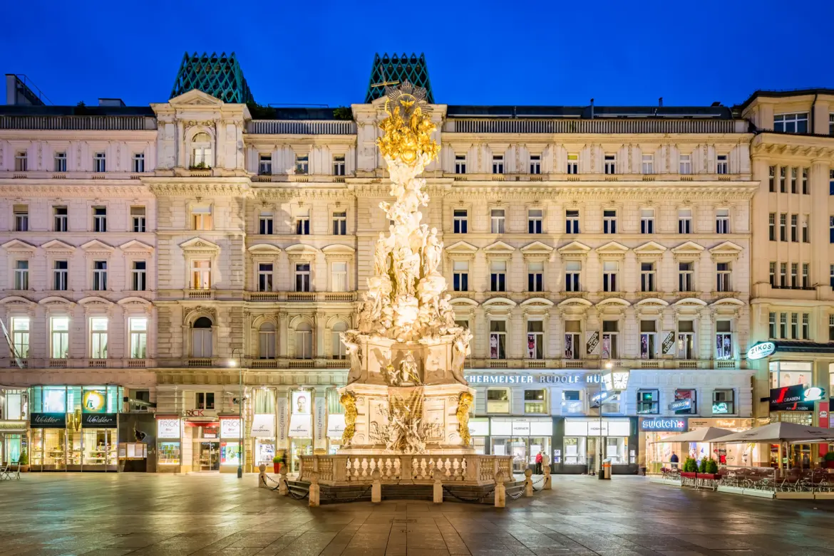 Plague Column illuminated at night on Graben in Vienna showcasing its Baroque details and sculptural composition against deep blue sky