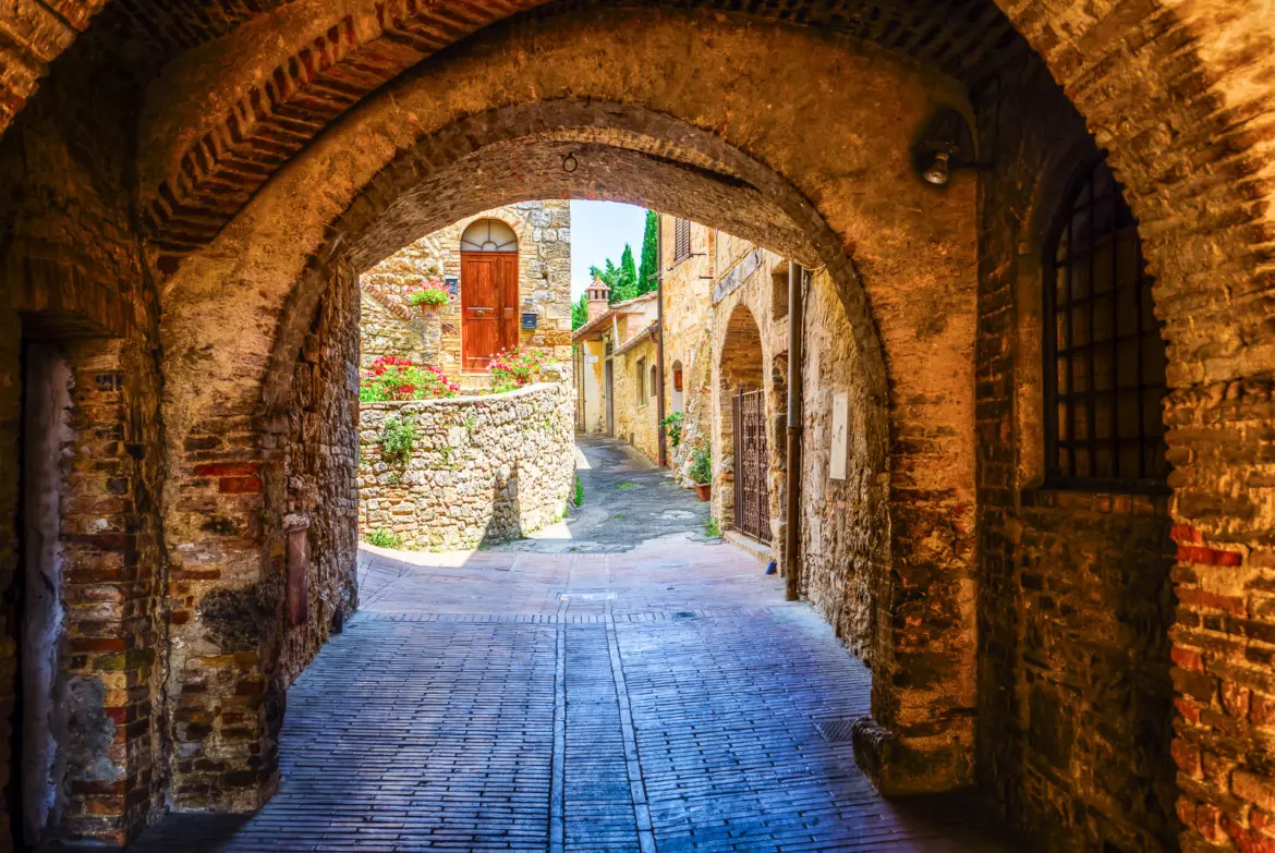 Charming cobblestone street framed by a medieval archway in San Gimignano’s historic center, capturing the timeless atmosphere of this Tuscan hilltop town