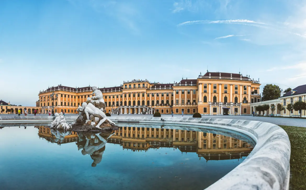 Schönbrunn Palace in Vienna reflected in a fountain with classical sculpture in the foreground, capturing the grandeur of the historic Habsburg summer residence