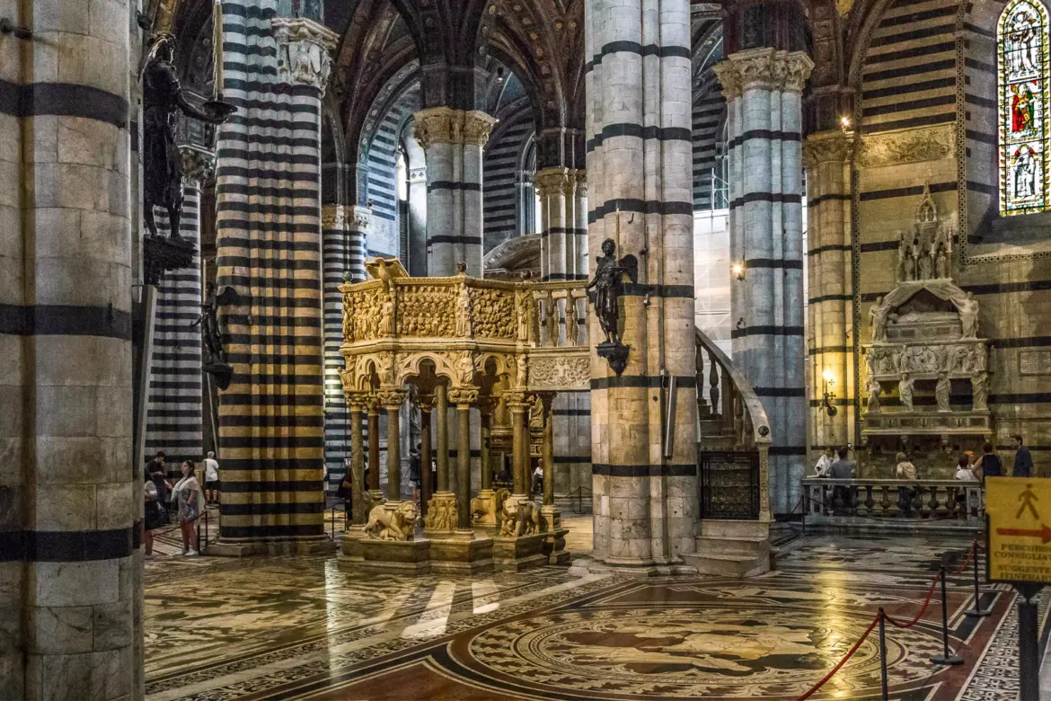 Interior of Siena Cathedral featuring Nicola Pisano’s sculpted pulpit, elaborate marble mosaic floors, and soaring striped columns