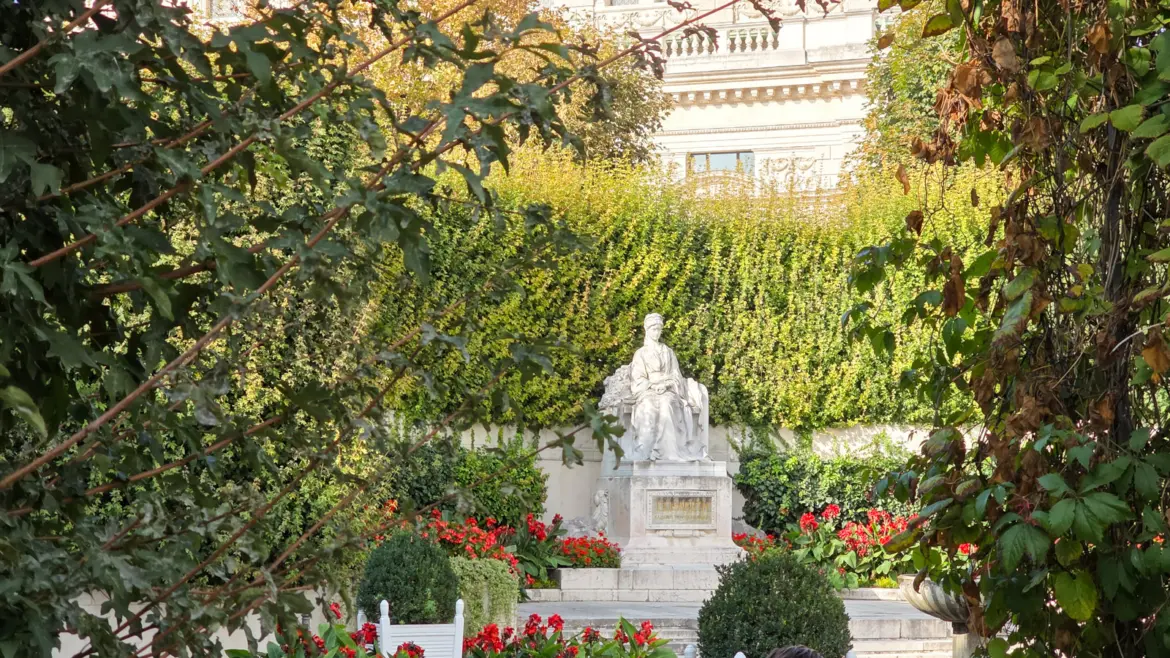 The Empress Elisabeth Monument honoring Sisi of Austria in Vienna’s Volksgarten, the white marble statue framed by lush greenery, red flowers, and the ivy-covered semicircular backdrop